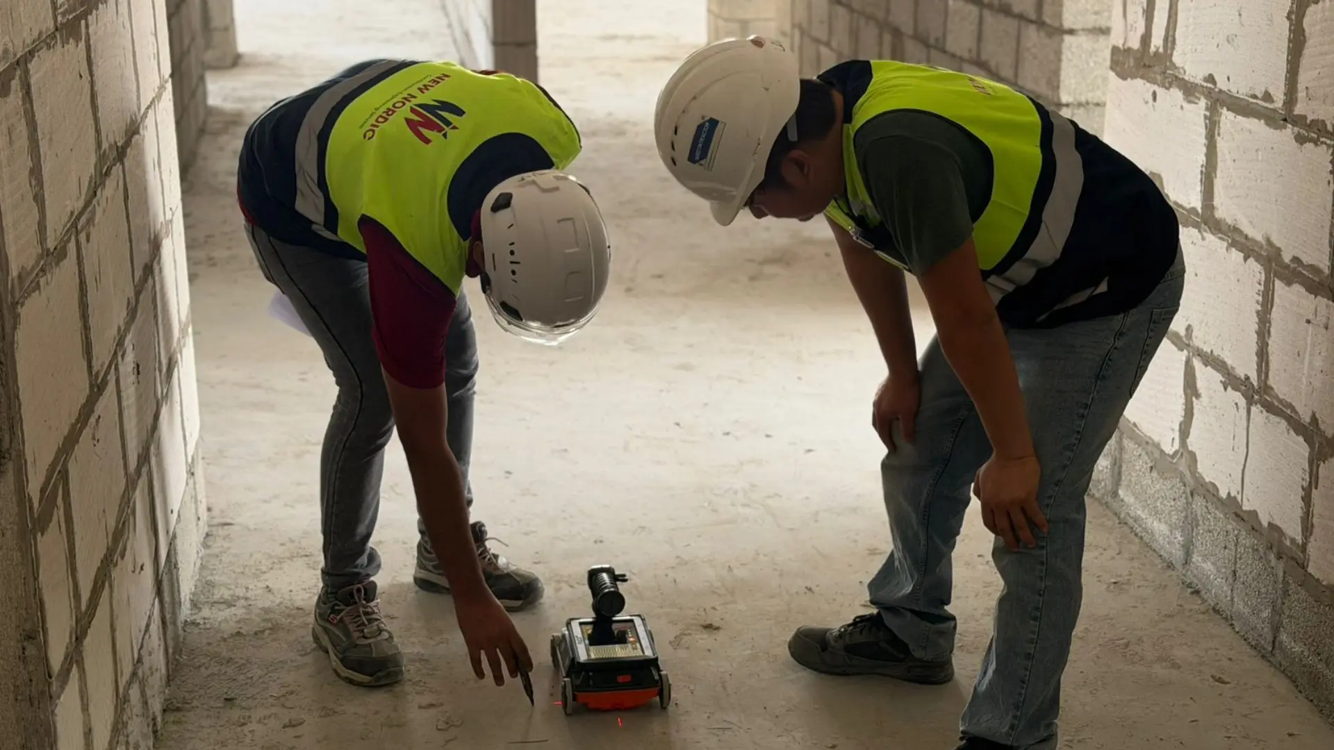 Two New Nordic engineers examining a ground-penetrating radar scanning device in an unfinished corridor