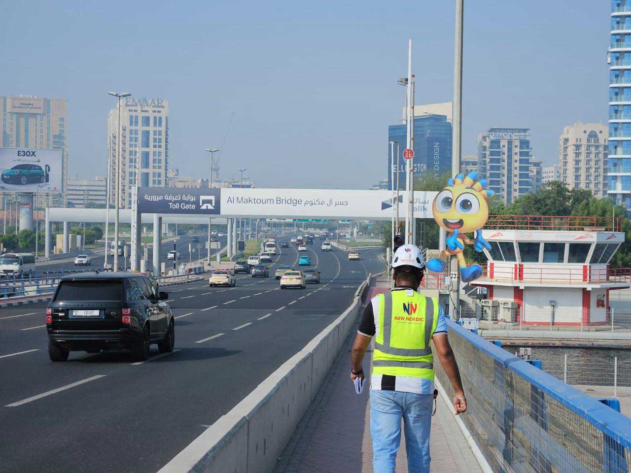 New Nordic engineer walking on a pedestrian walkway near Al Maktoum Bridge with the Dubai skyline behind