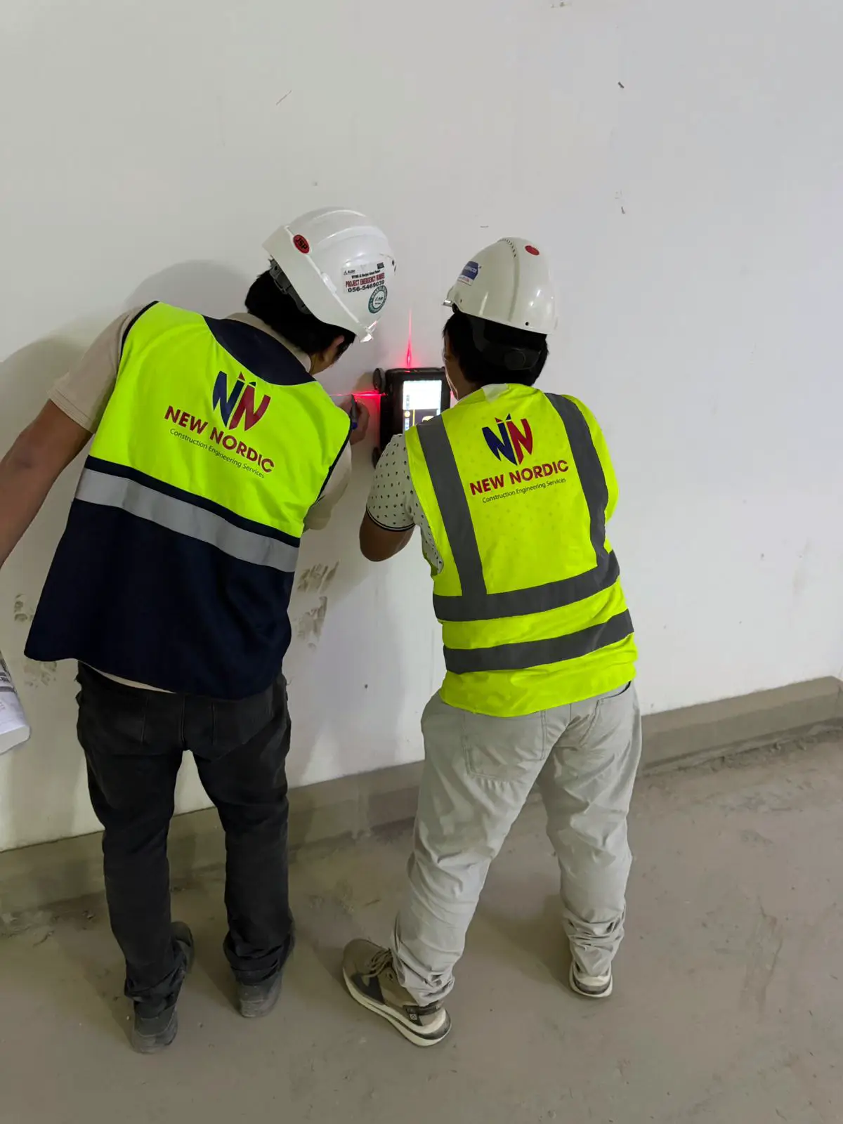 Two New Nordic engineers using a handheld scanning device with a laser pointer on an interior wall